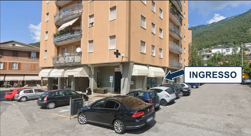 Il palazzo dell'ambulatorio visto dal piazzale: una freccia indica l'ingresso, sotto i portici, sul lato destro della facciata.